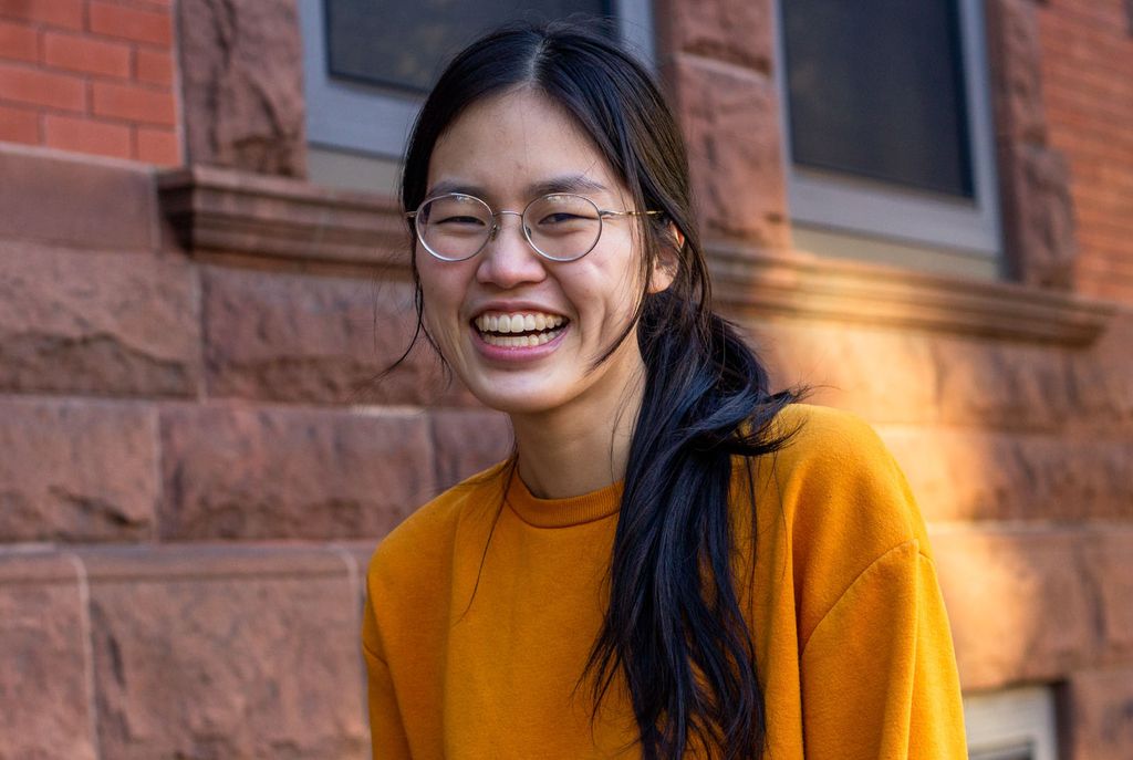 photo of Untangle Magazine creators Emily Wu, an Asian American woman wearing a deep yellow sweater. She stands near a brownstone and smiles to the camera.