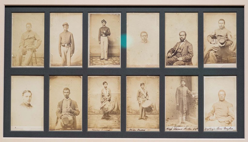 A series of twelve sepia photos of Black soldiers in the 54th Massachusetts Volunteer Regiment on display at Museum of African American History (MAAH) on Joy Street in Boston. The men wear dark soldiers uniforms, others wear suits, and a few hold drums.