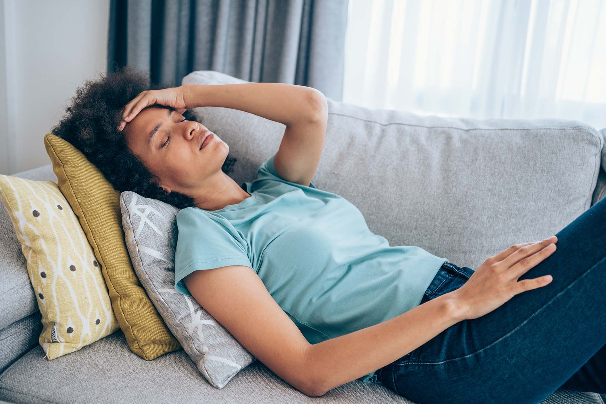 Photo of a young lighter skinned black woman lying on the couch and holding her head with her hand.