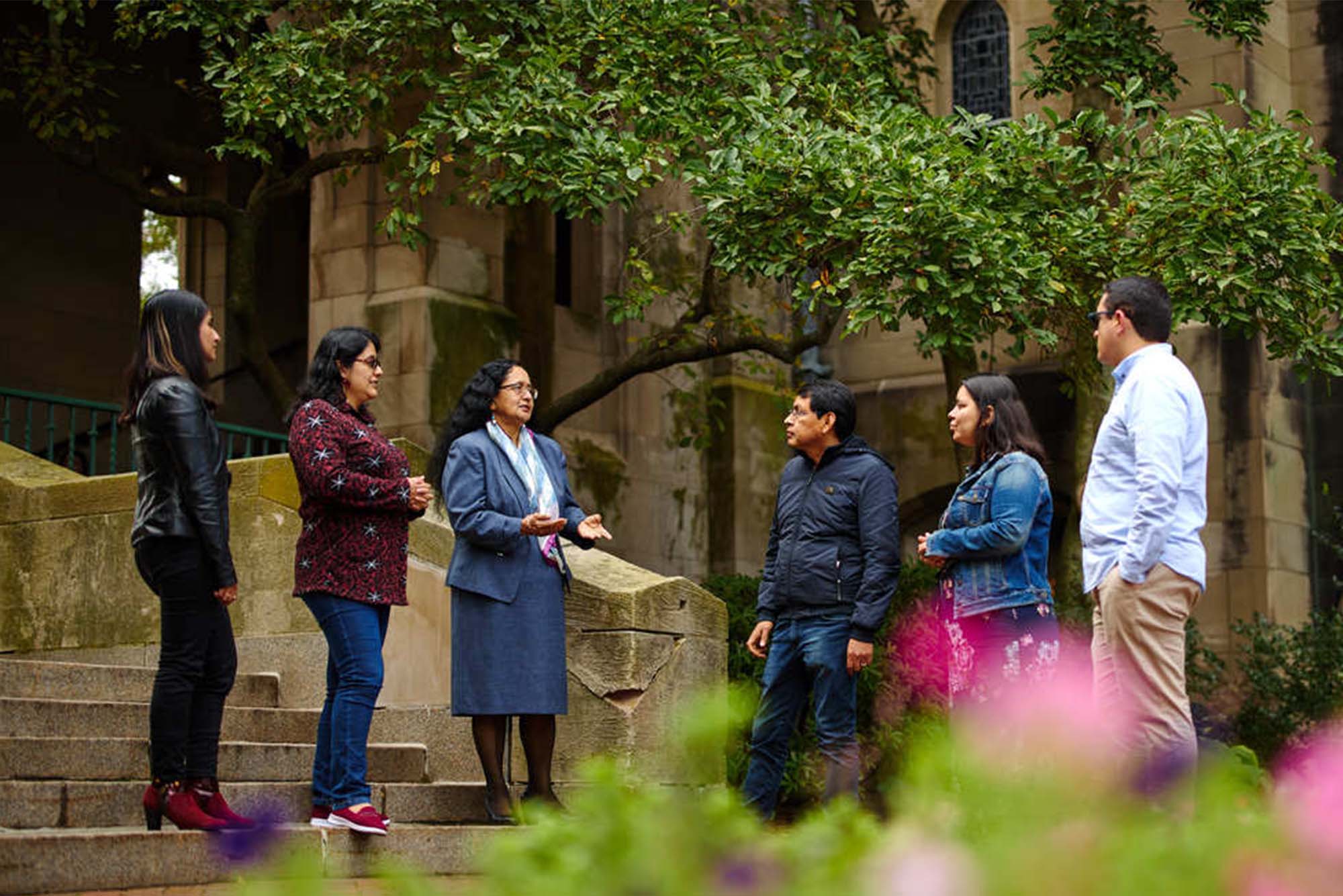 Multiple people stand in a semi circle in front of green trees on BU's campus in Boston MA