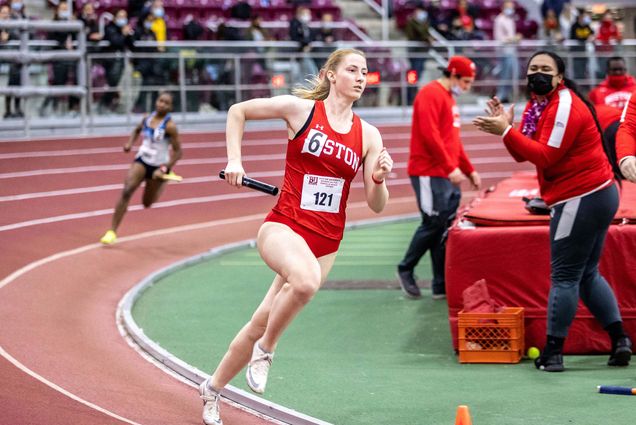 Kathleen Overbaugh runs the track with a baton in hand as someone races in close pursuit as onlookers cheer