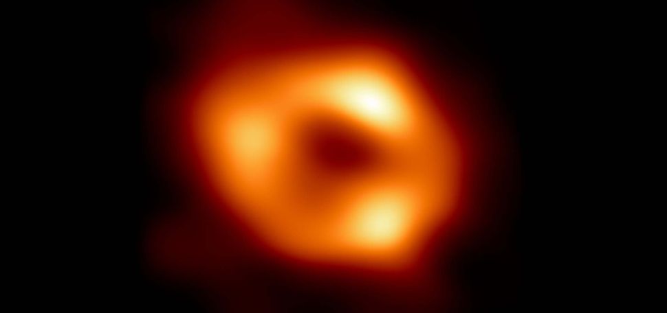 Image giving the first visual evidence of the presence of Sagittarius A*, the supermassive black hole at the center of our galaxy, captured by the Event Horizon Telescope (EHT) Collaboration. EHT Collaboration. In the image, a bright orange blob is seen, sort of resembling a donut, with three brighter yellow spots. The area around the orb is pitch black.