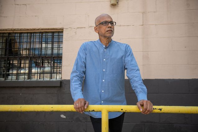 photo of André de Quadros, choir director and teacher of music in the BU prison education program, looking at the camera with a stoic expression. He wears black, rectangular glasses and a light blue collared shirt.
