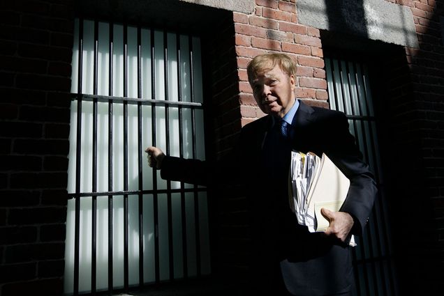 Photo of Bill Baird standing outside an old Charles Street Jail cell. An older man with blonde hair poses against a brick building with barred windows.