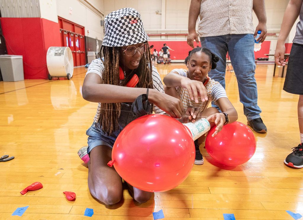 Imani Williams, 15 (front), and Ella Holloway, 15, work together to get their balloon-propelled rocket to work efficiently in the BU Academy gym, where rocket-inspired STEM activities were offered to high schoolers prior to the start of the NASA Downlink event with astronaut Bob Hines (ENG’97) in the GSU. 