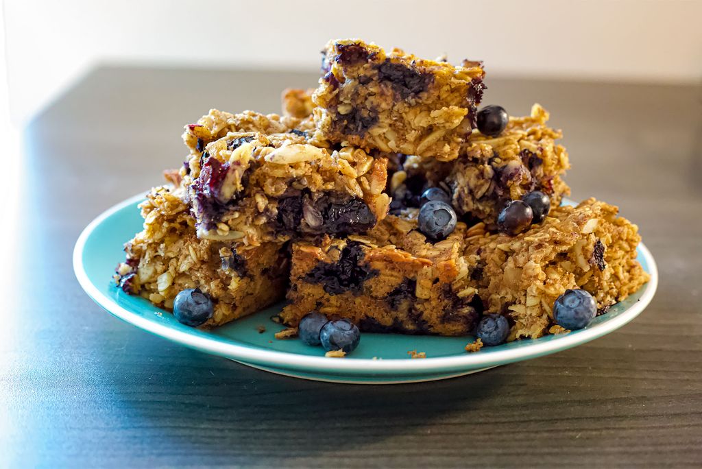 A plate full of blueberry breakfast bars with ginger and almonds sits on a wooden table