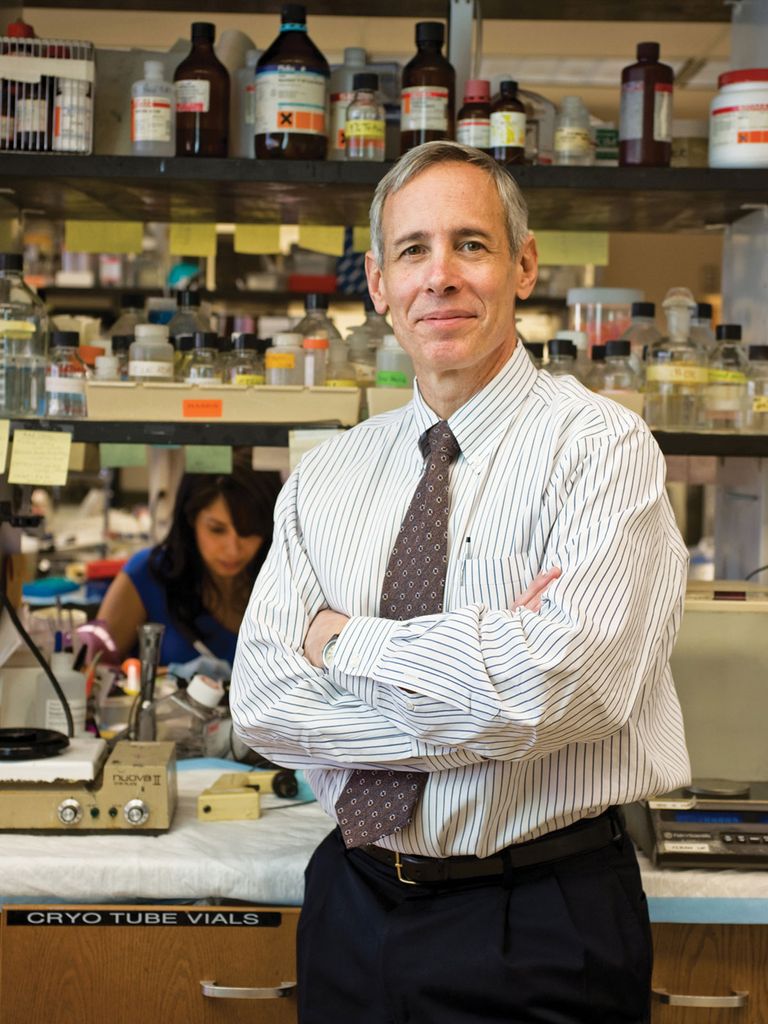 Photo of Burton Dickey, wearing a white button down shirt and purple tie. He stands in a lab and smiles and his arms crossed across his chest.