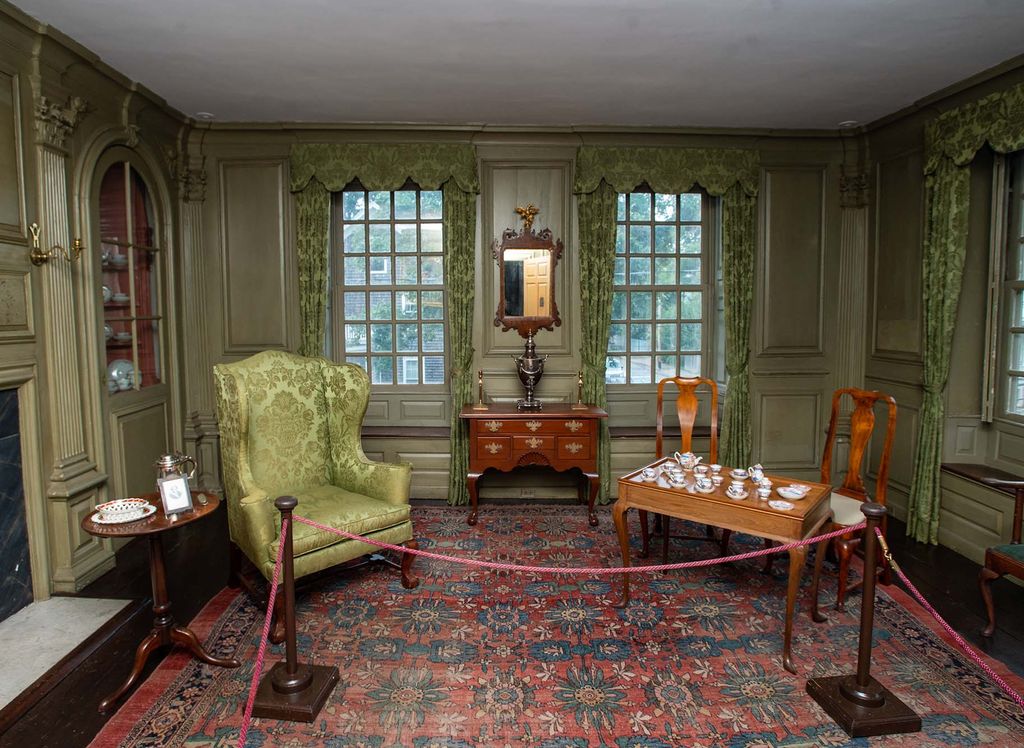 Photo: A large green themed room features ornate decorations and red and black rug, with a large green armchair to the left and a small wooden table with two chairs to the right.