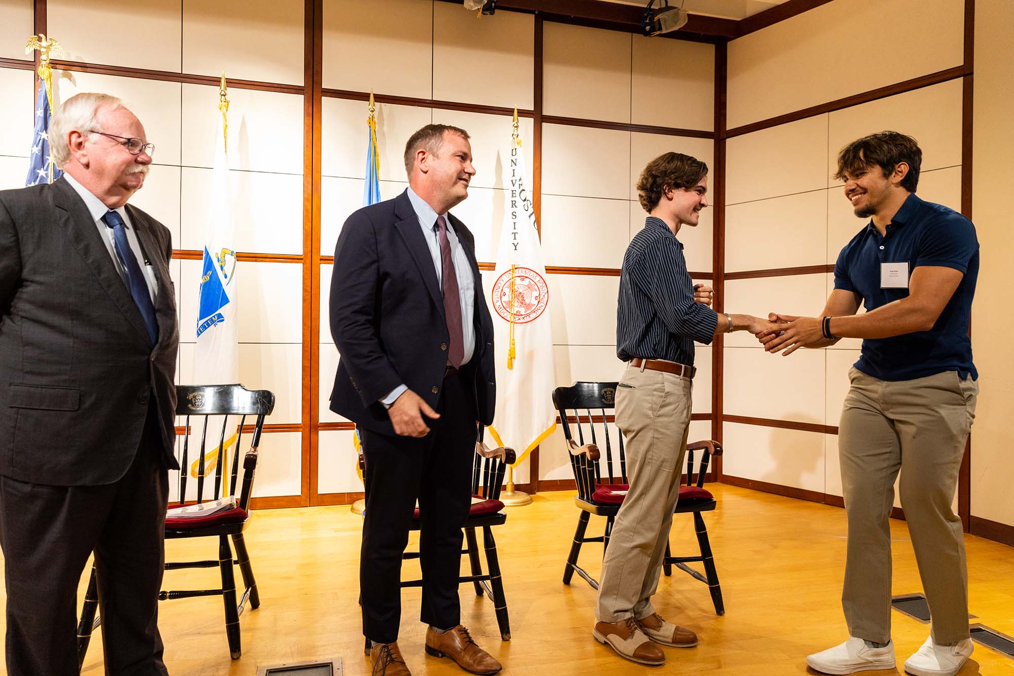 Photo of Angel Amaya (ENG’26). A young white man shakes hands with a student to his right as two officials, one being BU President Bob Brown, stand to his left.