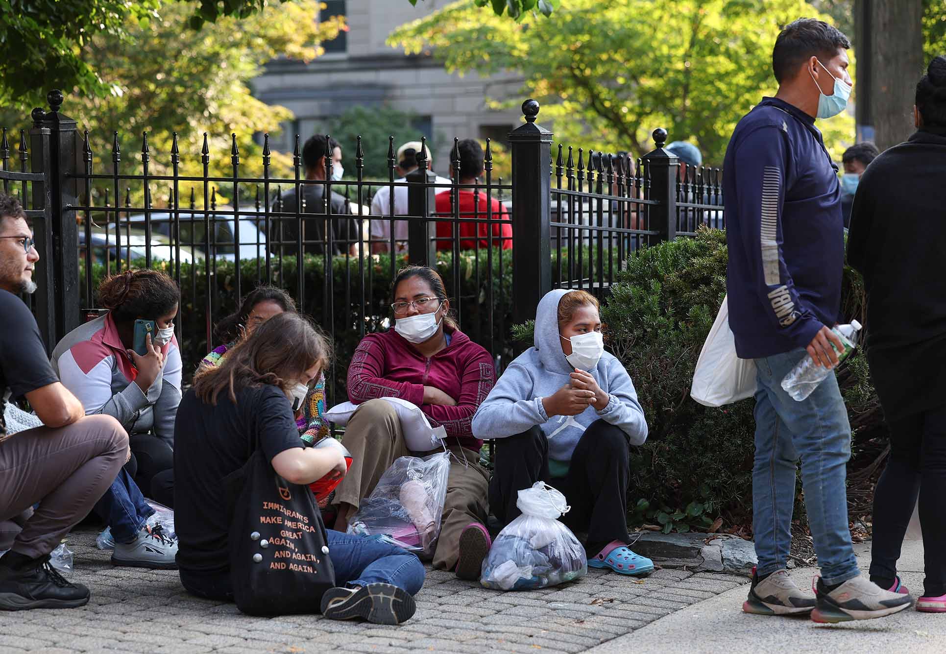 Photo: Migrants from Central and South America wait near the residence of US Vice President Kamala Harris after being dropped off on September 15, 2022 in Washington, DC. A group of masked migrants huddle and squat in front of a fence.