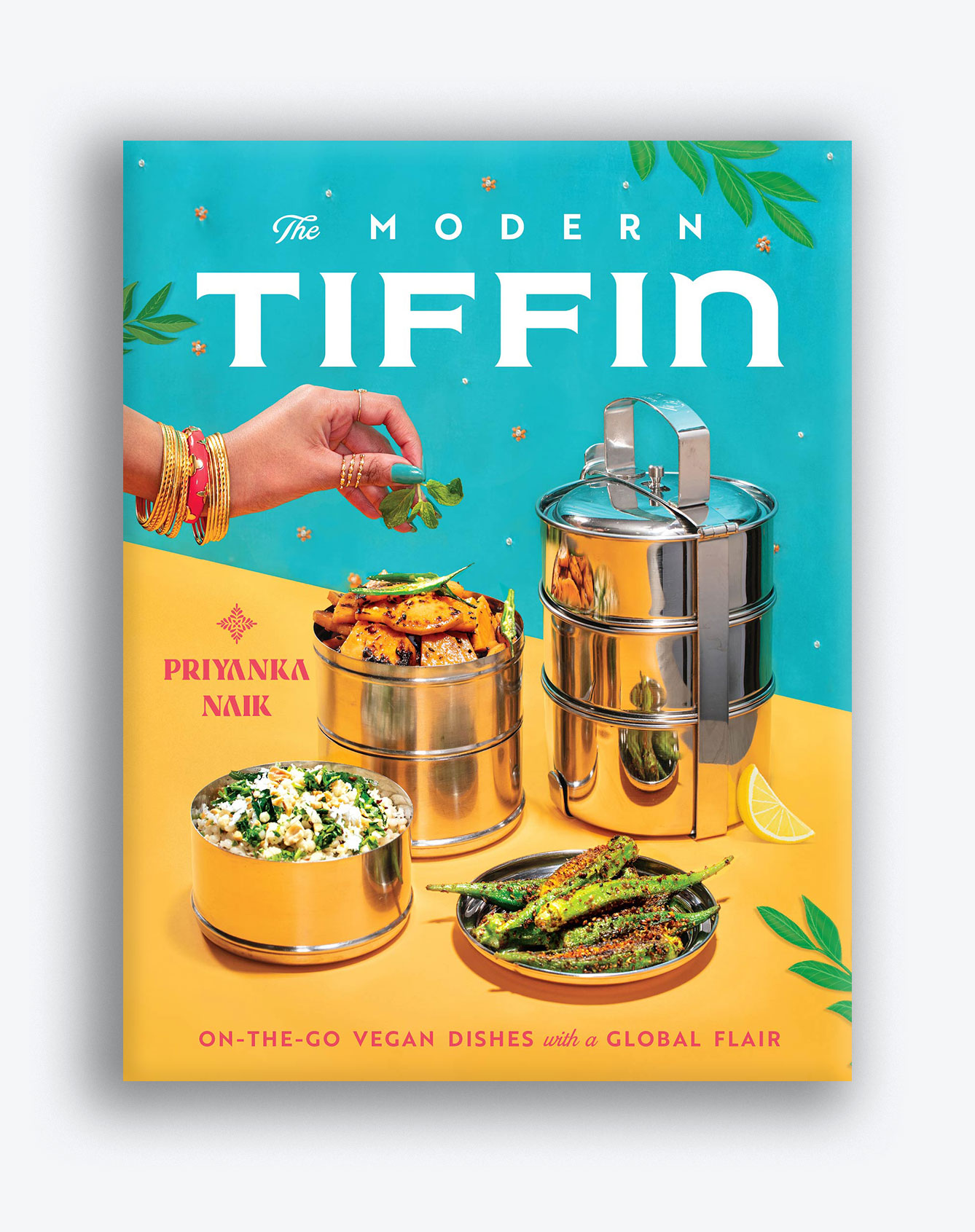 Photo of the cover of "The Modern Tiffin" by Priyanka Naik. The cover features two tiffins, one broken into its compartments, and a hand garnishing the food in one of the tiers. The background is bright teal and yellow.