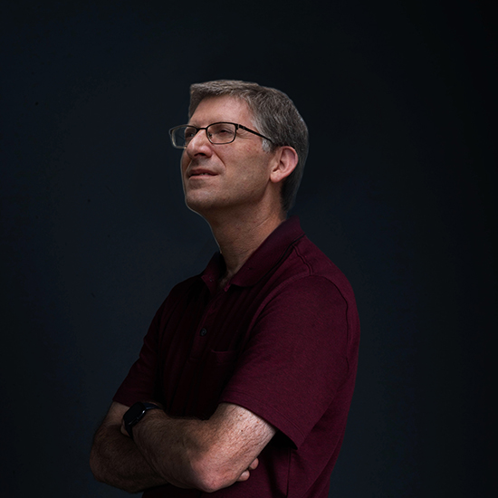 photo of Professor of Environmental Health, Jon Levy, as he poses in front of black backdrop looking off into distance with arms crossed.