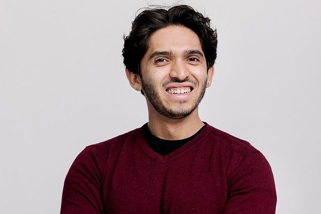 Photo: Headshot of Juan Ramirez, a Latinx man with black hair and wearing a black shirt and burgundy sweater, smiles and poses with arms crossed.