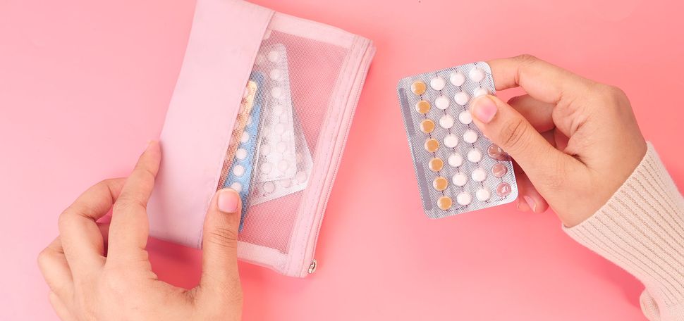 Photo of a person holding birth control pills close up. They hold a pack of slightly used pills over a pink background.