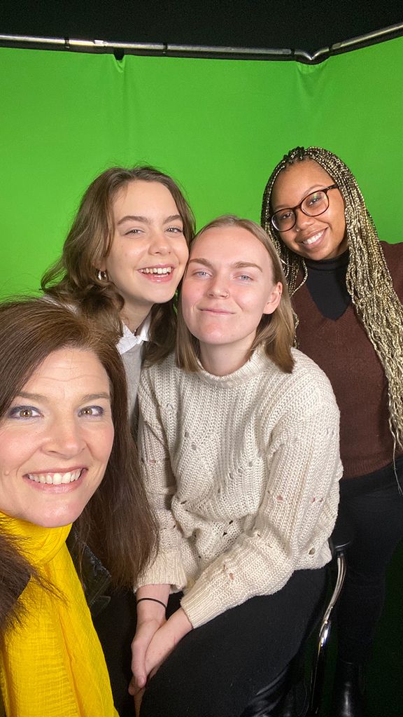 Photo of Lindsay (left) with three young woman in front of a green screen. They take a selfie together and smile for the photo.