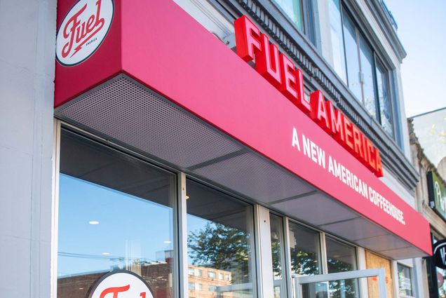 Photo: Exterior of Fuel America. Large red letters read "Fuel America" as the red canopy below reads "A new American Coffeehouse" both over the entrance for the shop.