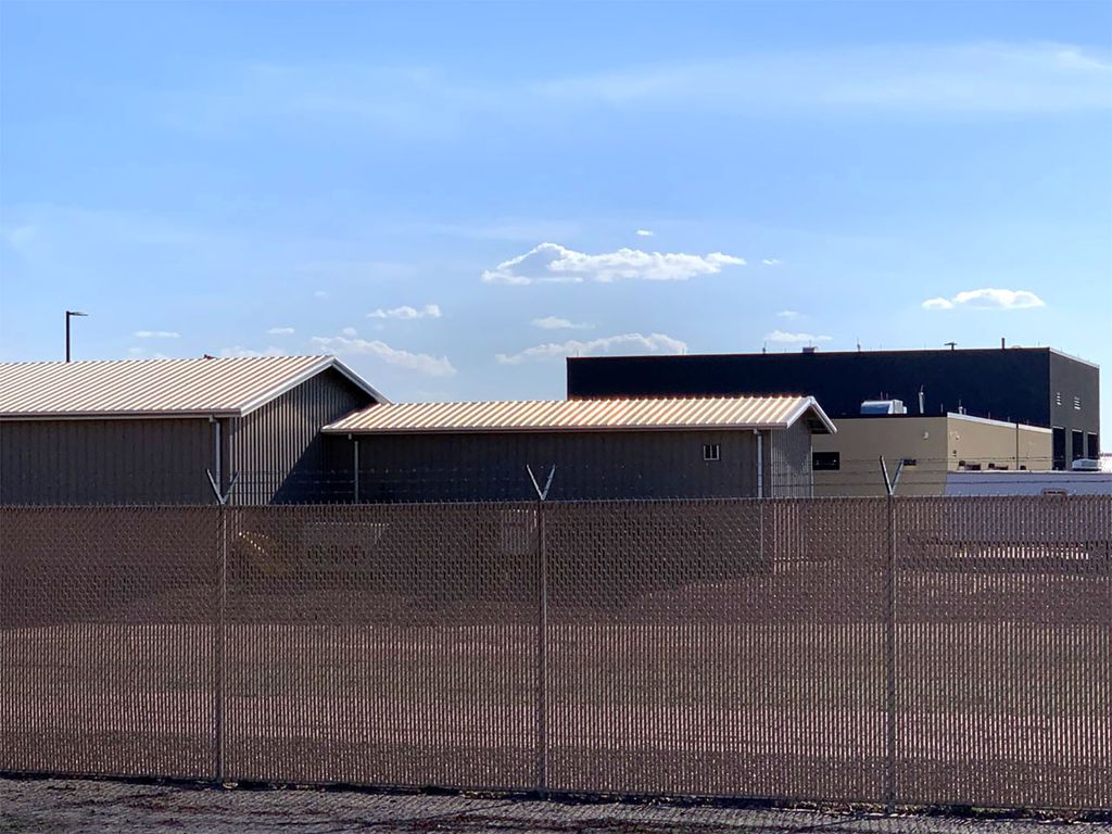 Photo of the Clint Border Patrol facility taken in 2019. The facility is hidden behind a metal fence. Blue sky is seen behind it.