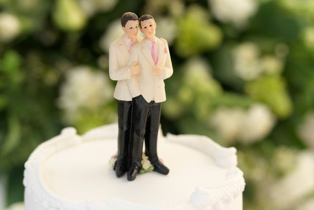 A wedding cake topper with two men in white suits