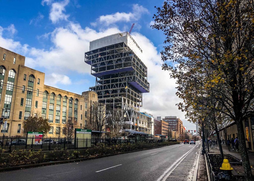 Photo of the Data Science building after the cantilevers have been removed, revealing the buildings outline that resembles a stack of books. The sky is bright blue with puffy white clouds and the trees have fall-colored leaves.