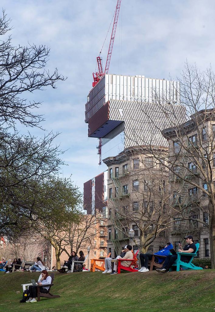 Photo: Students take advantage of a beautiful afternoon on BU Beach April 11. A large crowd of students hang out on a green lawn. The Data Science building can be seen looming in the background with it's reflective mirror sides.