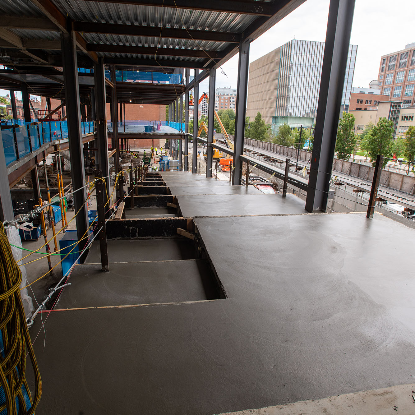 Photo: Interior of the Center for Computing and Data Science as work continues to be done. A large set of stairways set in cement are shown next to a large set of glass walls tot he right. Various construction workers can be seen working around the scene.