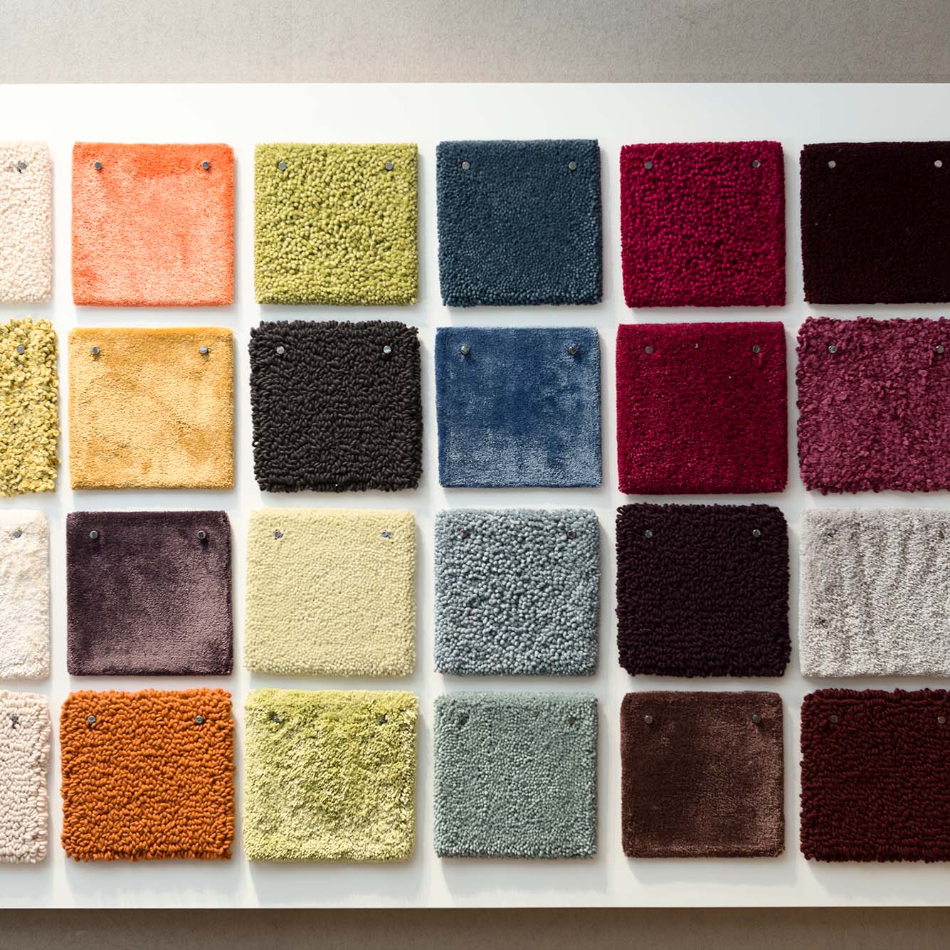 Photo of a selection of Samples of color for carpet coverings. A white board shows squares of various-colored carpet swatches.