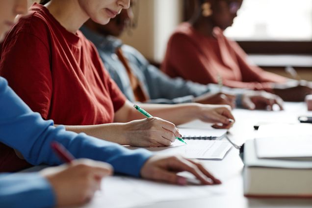 A row of college students in a college classroom taking notes with paper and pencil