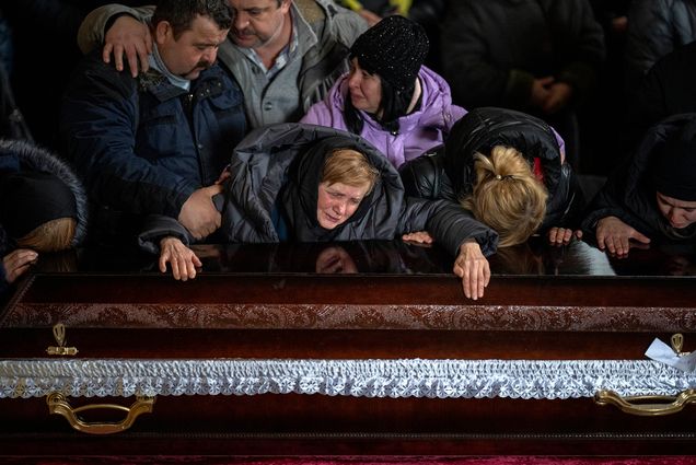 Photo: A Ukrainian woman and her family members gather over a closed casket at a funeral for a Ukrainian solider who died during the Russian occupation of Ukraine. They are wearing heavy outwear indicating it is cold.