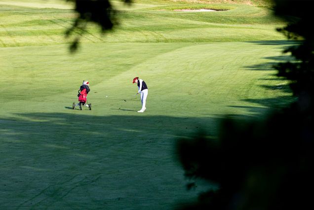 Photo: Alice Fan of the BU Women's Golf team hits a fairway shot at a recent match. She stands alone over her ball on the large green expanse, club in hand