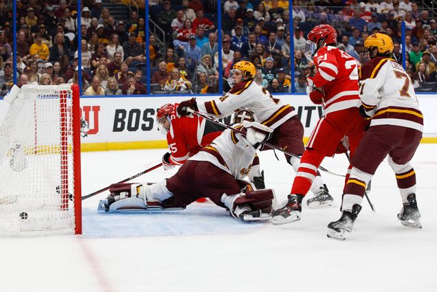 Photo: The Boston University Terriers play the Minnesota Golden Gophers during game one of the 2023 NCAA Division I Men's Hockey Frozen Four Championship Semifinal at the Amaile Arena on April 6, 2023 in Tampa, Florida. Multiple hockey players in full equipment clash in front of a goalie doing the splits. (Photo by Rich Gagnon/BU Athletics)