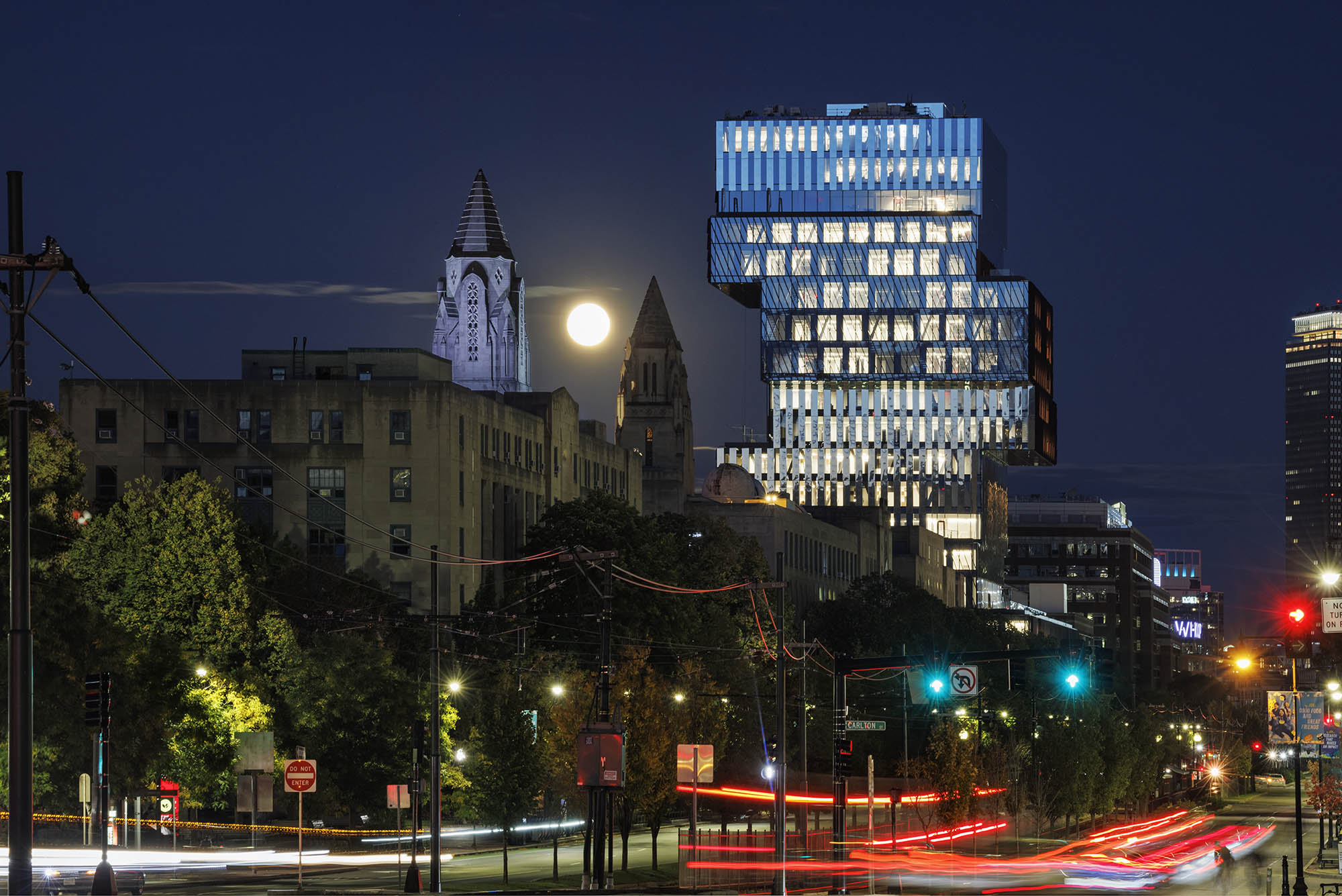 Photo: View of the CDS building from Commonwealth Ave on October 9, 2022. Nighttime stock campus photo of Boston University campus shows street-view of cars and pedestrians on BU's campus. The city and CDS building can be seen brightly lit against the night scene.