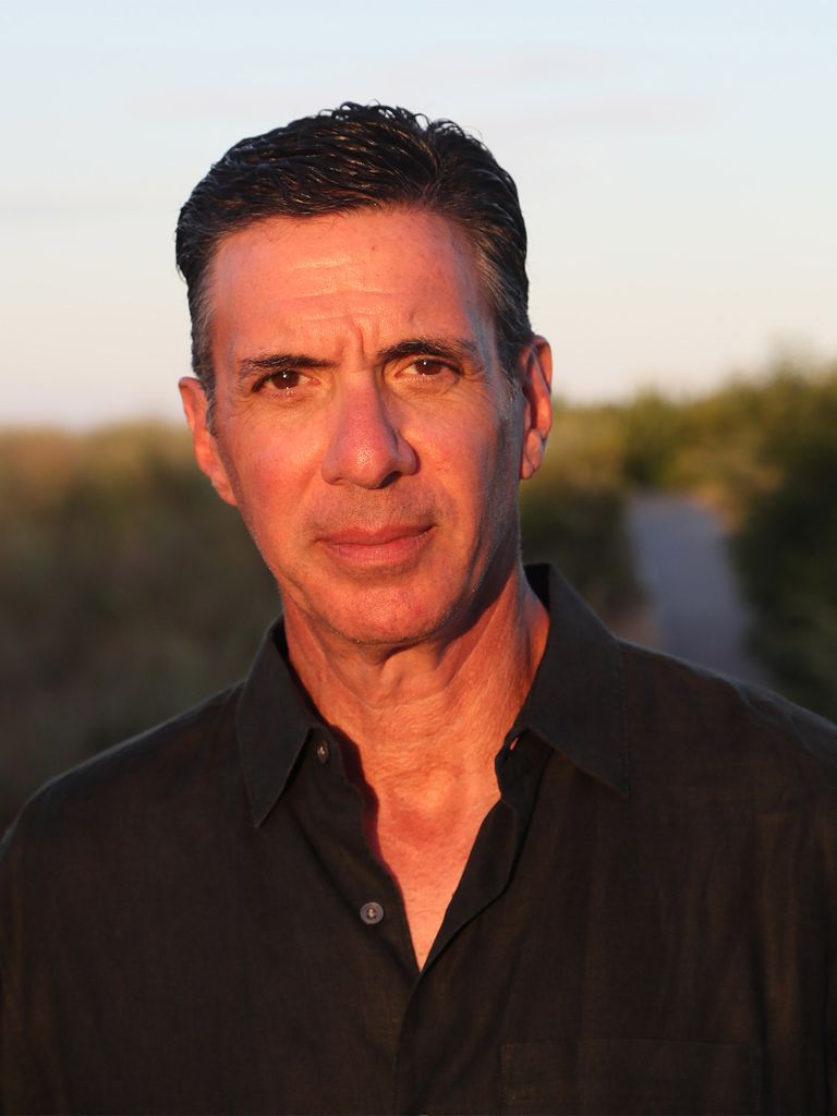 Photo: A white man with short hair wearing a collared v neck shirt poses for a headshot photo.