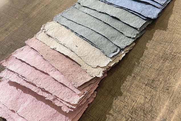 Photo: An array of re-purposed paper made into various colors is laid flat on a wooden table.