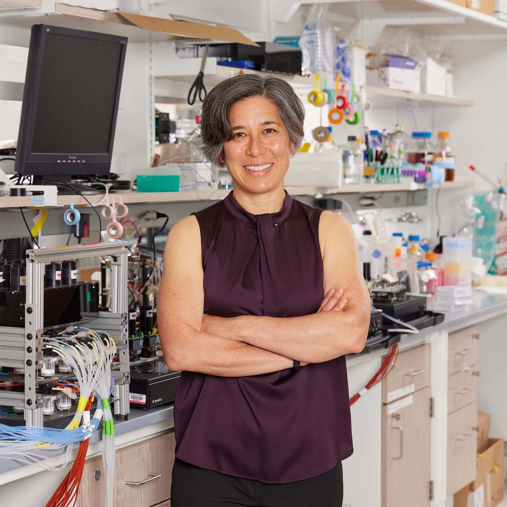 Photo: Elise Morgan stands with arms crossed in a laboratory of some kind with instruments and technology surrounding her