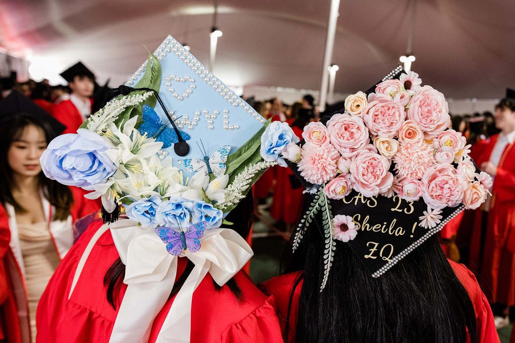 Photo: Two graduation caps decorated with flowers and words. The one on the left has blue flowers and background where the one on the right utlizes the black background of the cap and uses pink flowers.