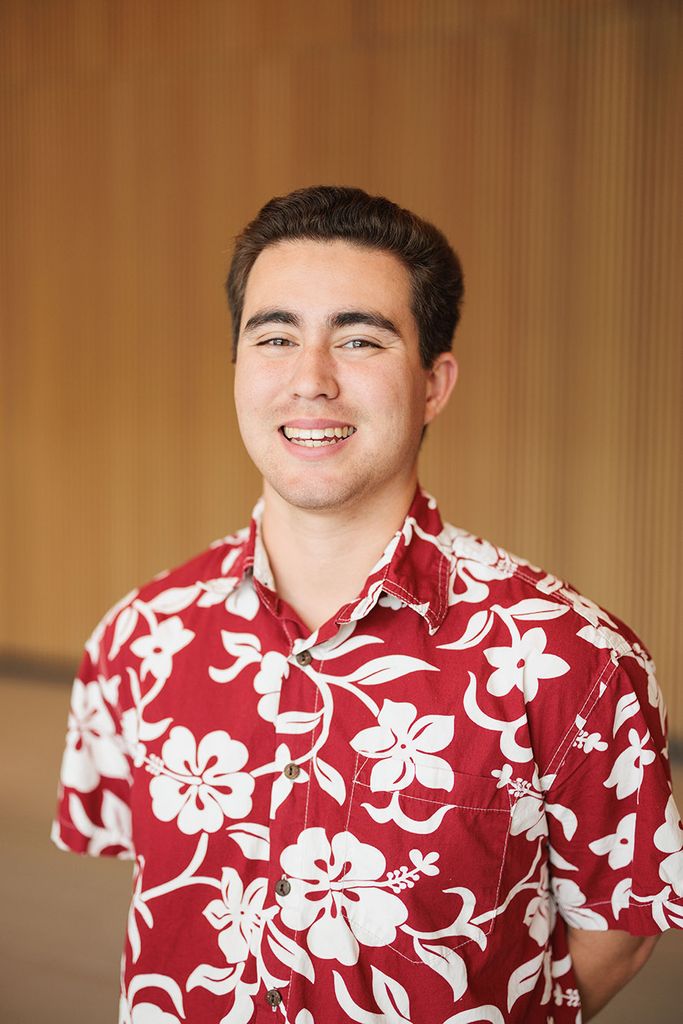 Photo: Edward Wong, a young man with dark brown hair and wearing a red floral Hawaiian0themed collared shirt, smiles and poses for the camera.