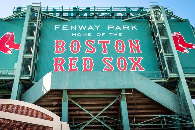 Photo: view of the historic architecture of the Fenway Park Stadium in Boston, Massachusetts, USA showcasing its sings and red brick walls on a sunny winter day. Text reads "Fenway Park, Home of the Boston Red Sox"