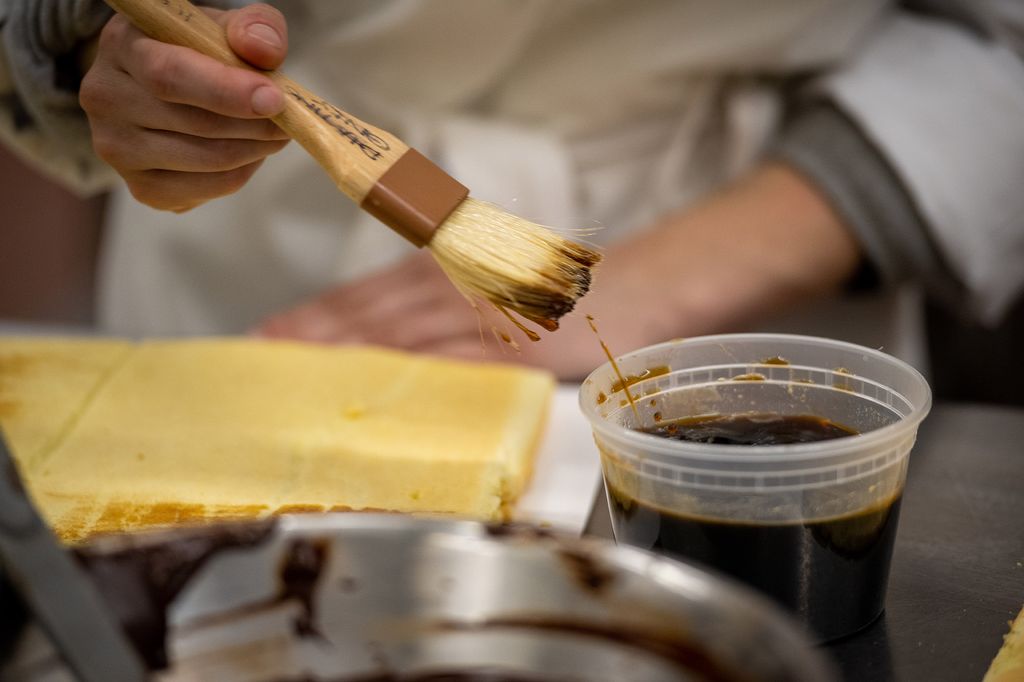 Photo: Zoomed in action shot of a hand adding coffee with a baking brush to a nut-free Japonaise Roule.