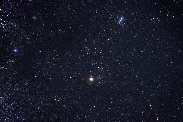 Photograph of the constellation Taurus made by the avid astrophotographer Akira Fujii. In the photo, tiny white dots, stars, fill the image, with a brighter, reddish dot towards the bottom right, which is Taurus.