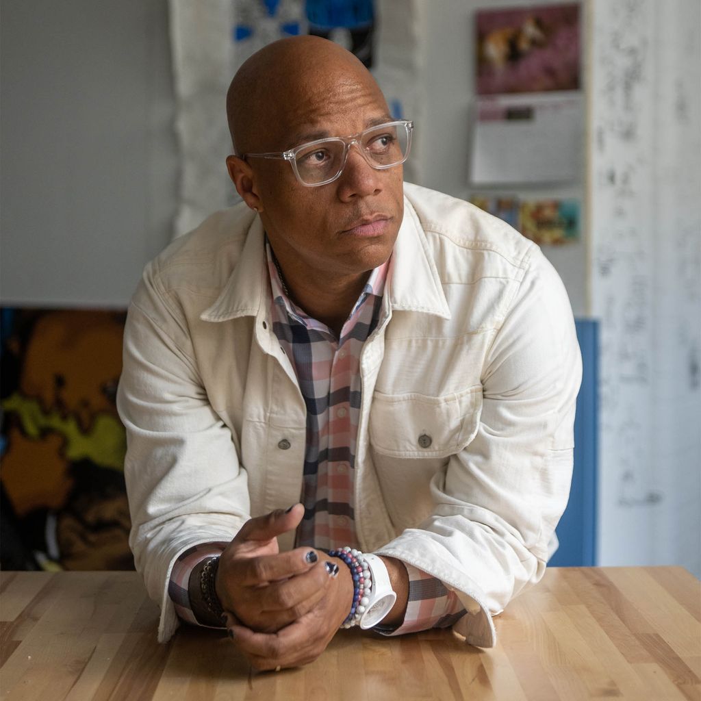 Photo: Joel Christian Gil, a middle aged bald black man wearing a white shirt and glasses, stares off into the distance in this serious portrait. Gill is the Associate Professor of Art; Chair, Department of Visual Narrative at Boston University College of Fine Arts