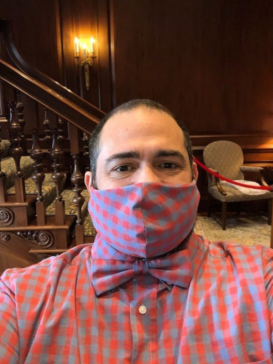Photo of Jesus Nater with a matching mask, bowtie, and button down with a muted blue and red checkered pattern.