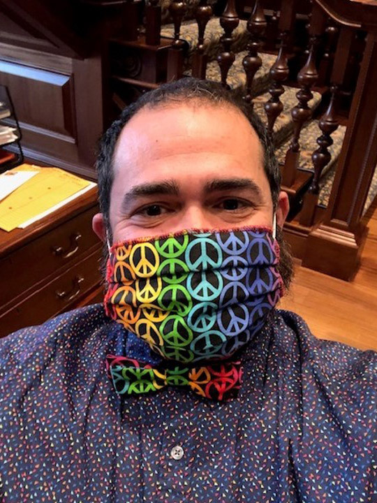 Photo of Jesus Nater with a matching mask and bowtie that is black with rainbow peace signs on it.