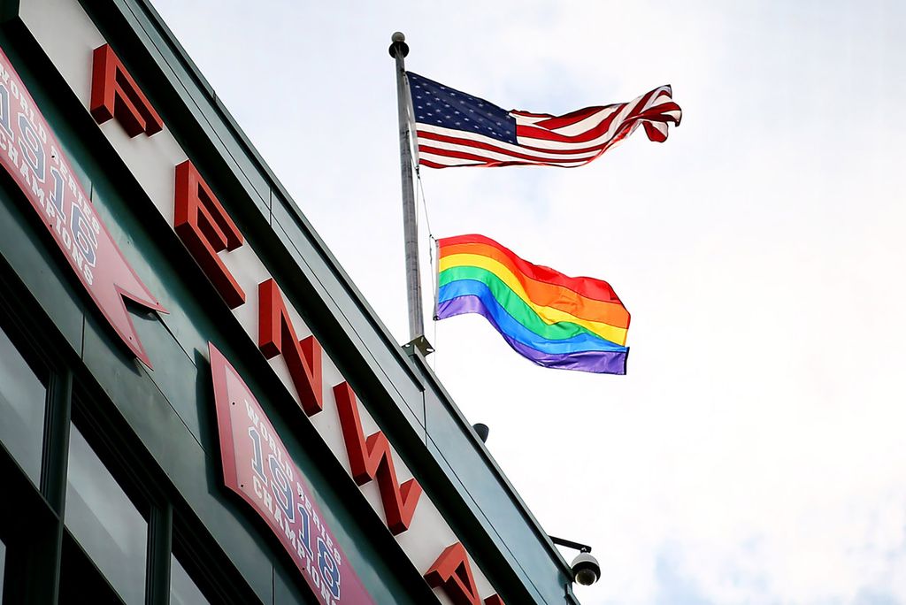 Photo: American flag and pride flag on top of Fenway outer building, waving into the wind.