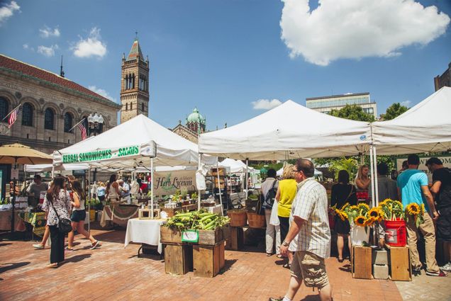 Photo: A man walks in front of large white tents filled with produce and various other vendors.
