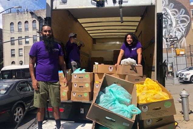 Photo: 3 people stand in the back of a large moving truck filled with groceries that will be delivered to a food pantry
