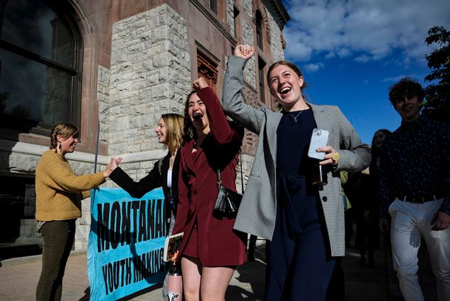 Photo: Youth plaintiffs in the climate change lawsuit, Held vs. Montana, arrive at the Lewis and Clark County Courthouse, on June 20, 2023, in Helena, Montana. A group of young people wearing business casual wear smile and cheer as they walk towards a courtroom building.