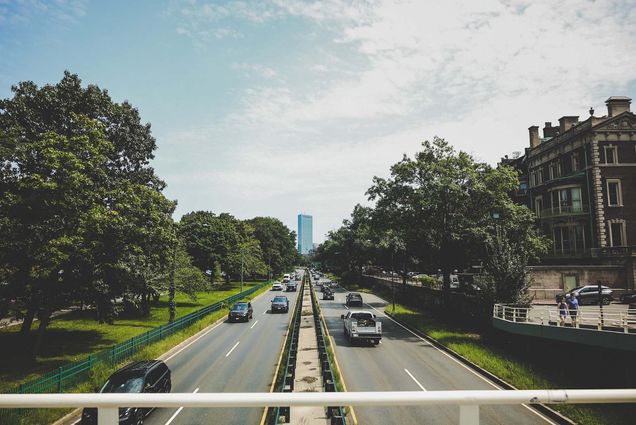 Photo: Image of Storrow Drive in Boston, MA. A two-lane local highway is shown with both directions of traffic on a sunny day. the Boston city skyline can be seen in the distance and Boston University buildings can be seen to the right.