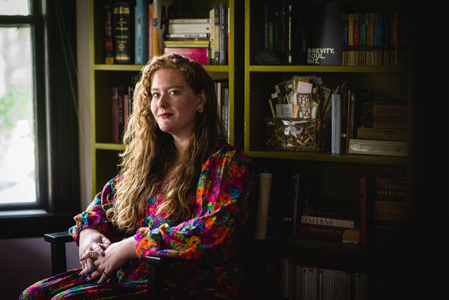 Photo: A person in a colorful outfit sits in front of a wall of books in an old home in Somerville. MA