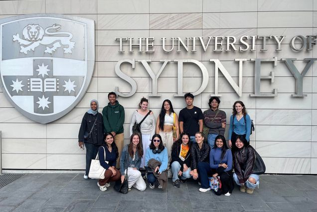 Photo: A group of college students in casual attire stand in front of a sign that reads "University of Sydney"