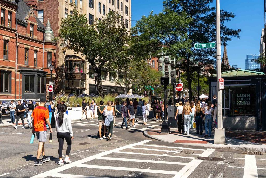 Photo: Small groups of people walk down an urban street lined with red brick brownstones and iron fences